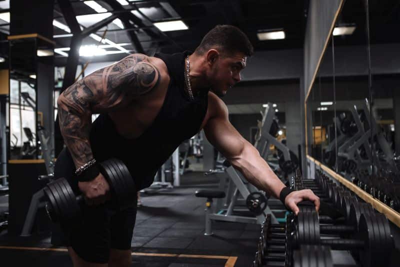 Strong tattooed bodybuilder working out with heavy dumbbells at the gym